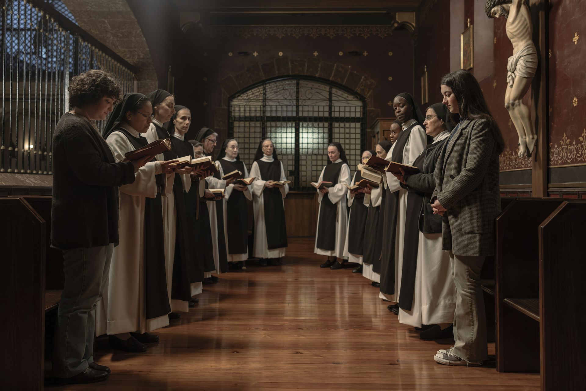 Un grupo de monjas cantan con una mujer y una adolescente en sus extremos.