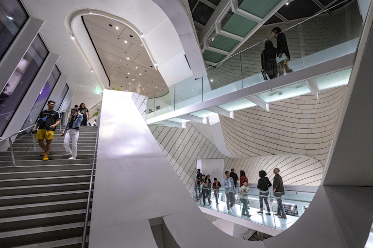 People mill around a very modern and artistic-looking stairwell and catwalk.