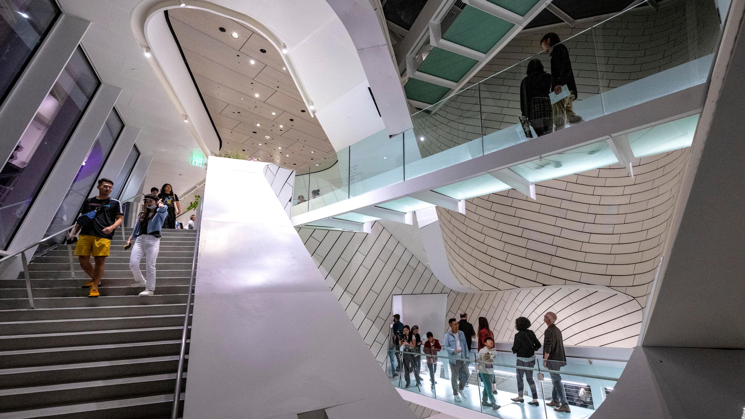People mill around a very modern and artistic-looking stairwell and catwalk.