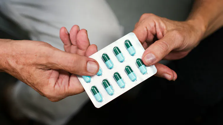 A blister pack of medication capsules changing hands