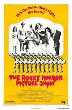 Un cartel amarillo dice 'The Rocky Horror Picture Show' y un coro de lo que parece patear cubos se encuentra debajo de un grupo de personas, una de las cuales tiene el pelo largo y blanco.