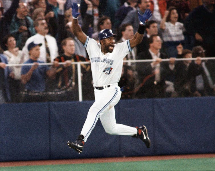 La fiebre de los Azulejos está surgiendo mientras Canadá se prepara para la Serie Mundial por primera vez en 32 años. 1 Un hombre negro con uniforme de béisbol blanco y azul salta en el aire en celebración mientras corre por las bases.