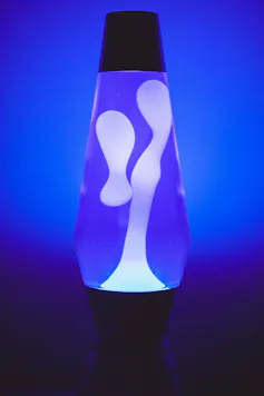 A lava lamp with white gel blobs in it on an indigo blue background.