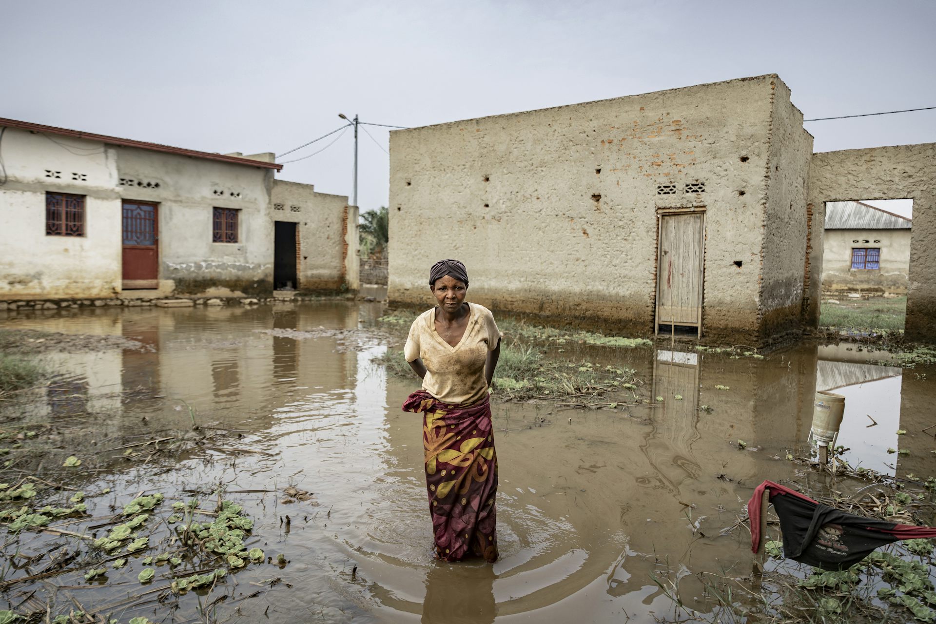 A woman stands inside her compound, in floodwaters up to her knees