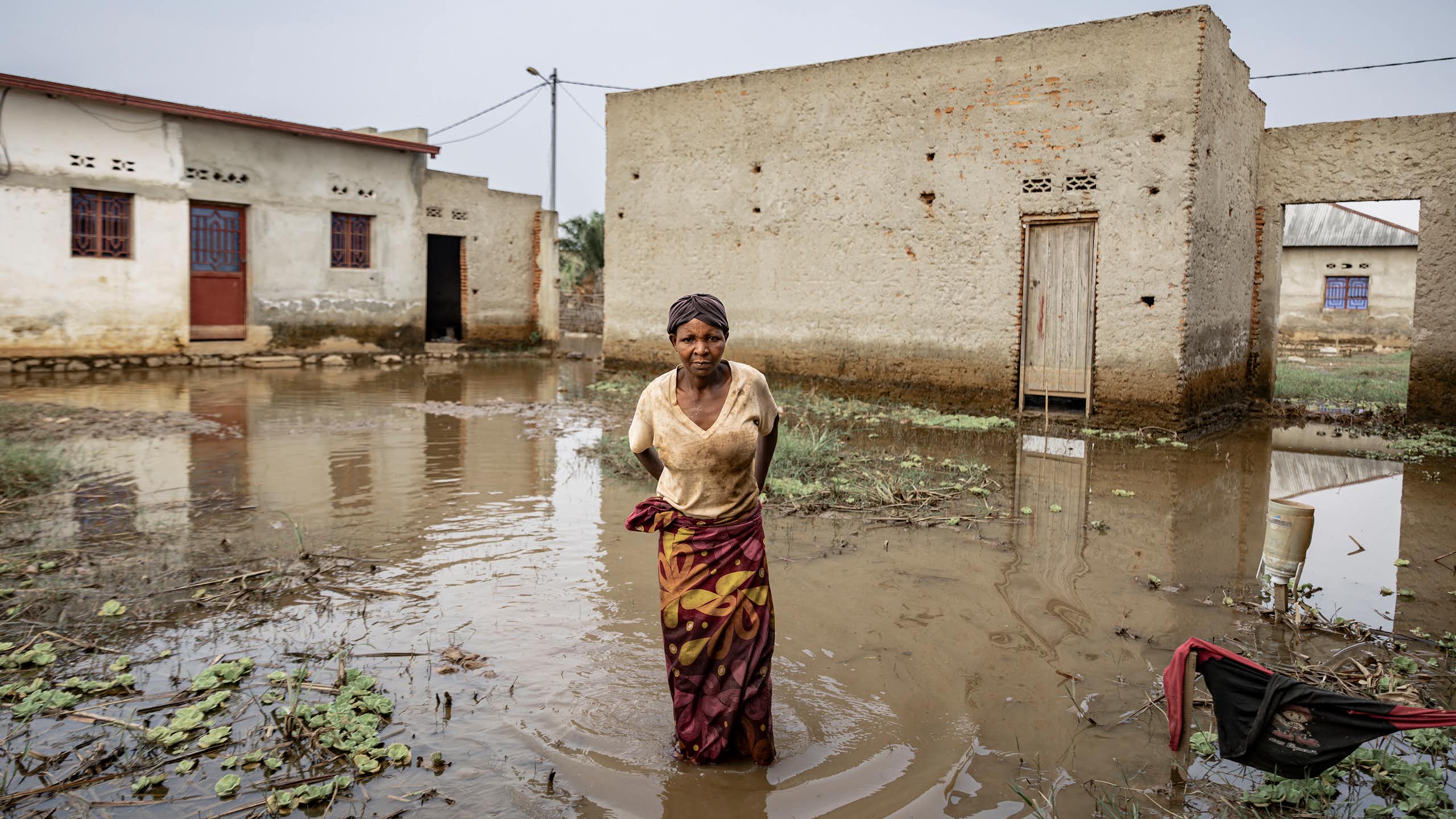 A woman stands inside her compound, in floodwaters up to her knees