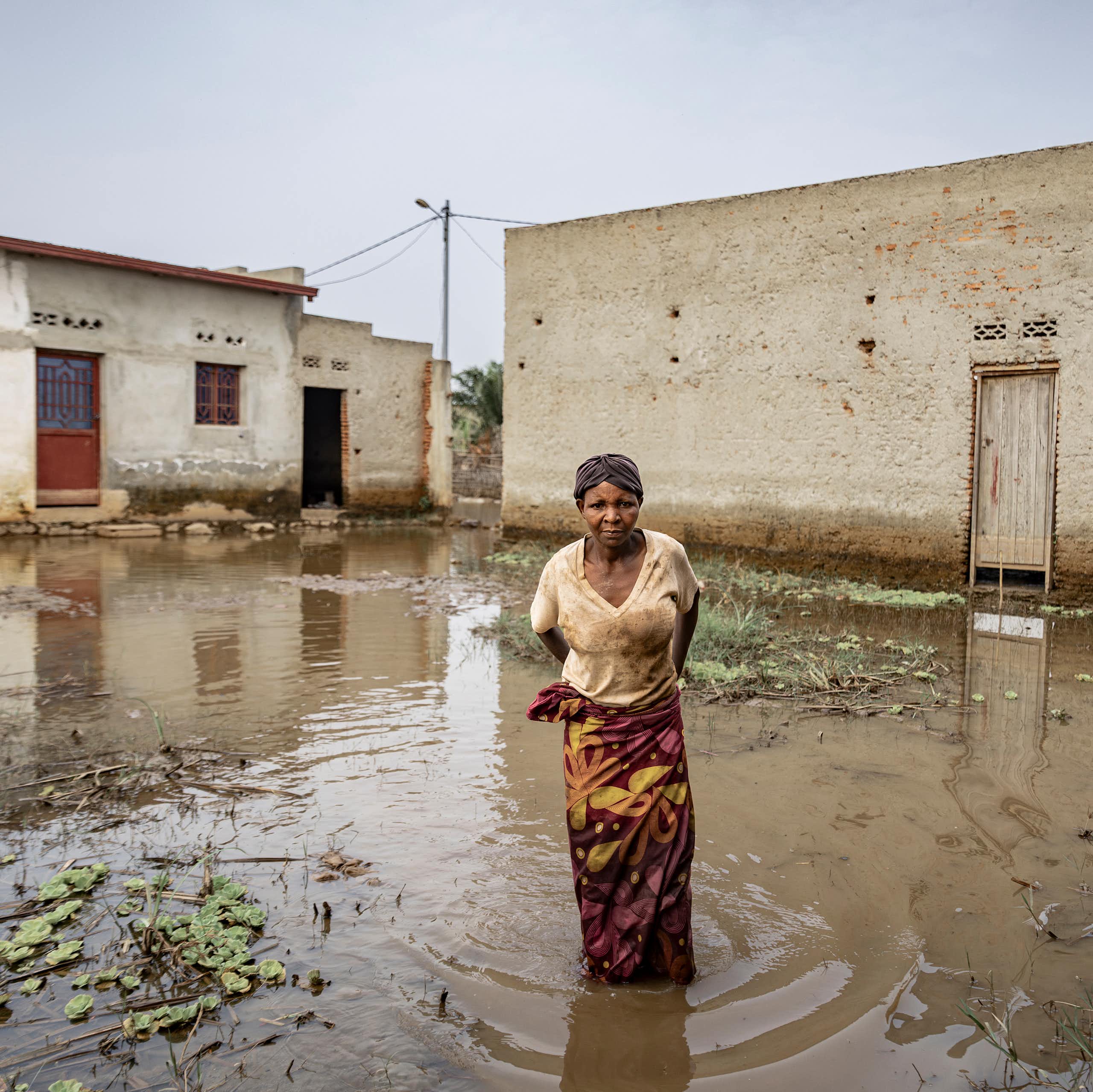 A woman stands inside her compound, in floodwaters up to her knees