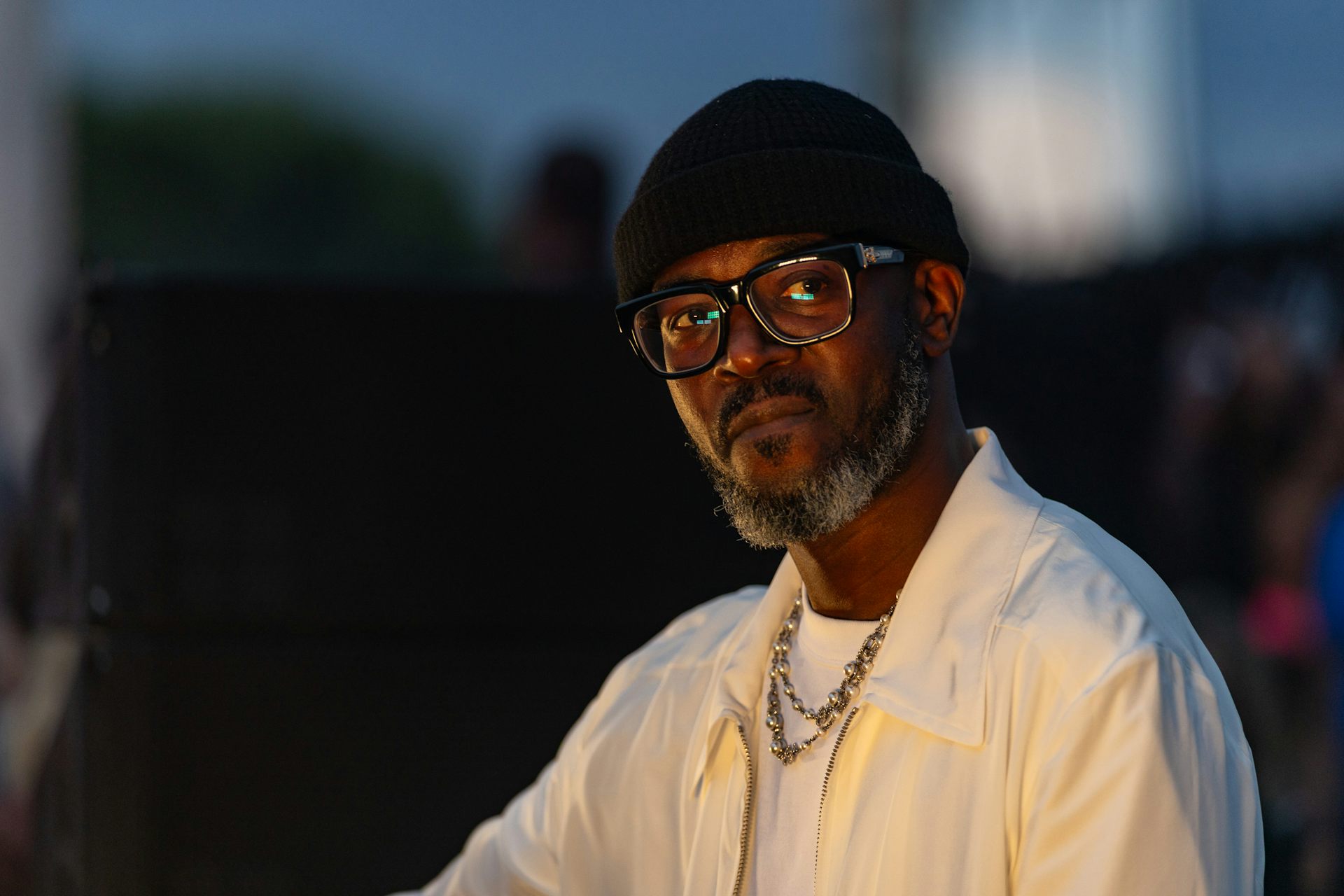An African man in a beanie and glasses looks ponderous in a photo.