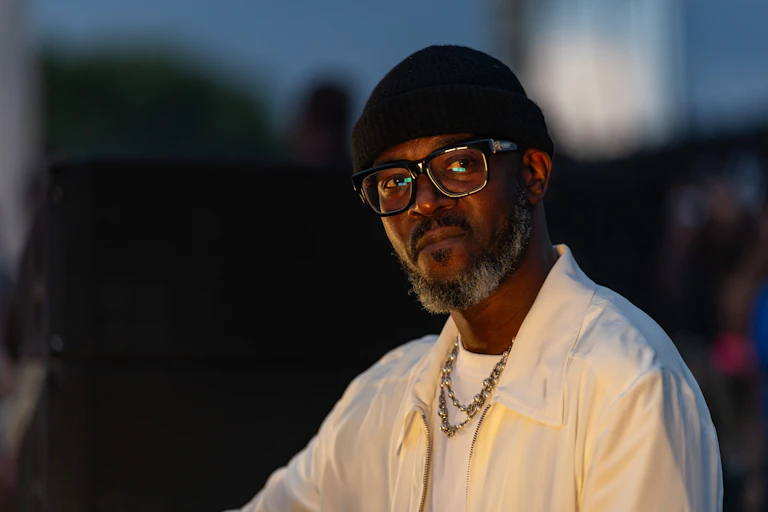 An African man in a beanie and glasses looks ponderous in a photo.