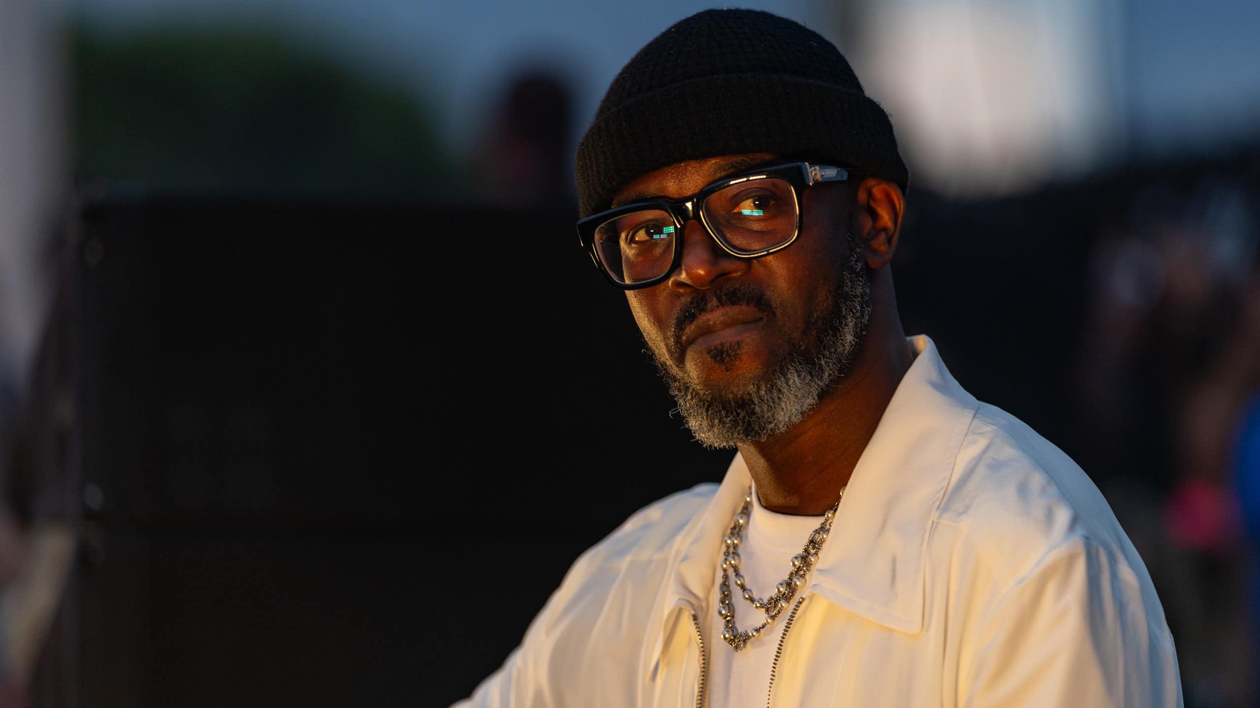 An African man in a beanie and glasses looks ponderous in a photo.