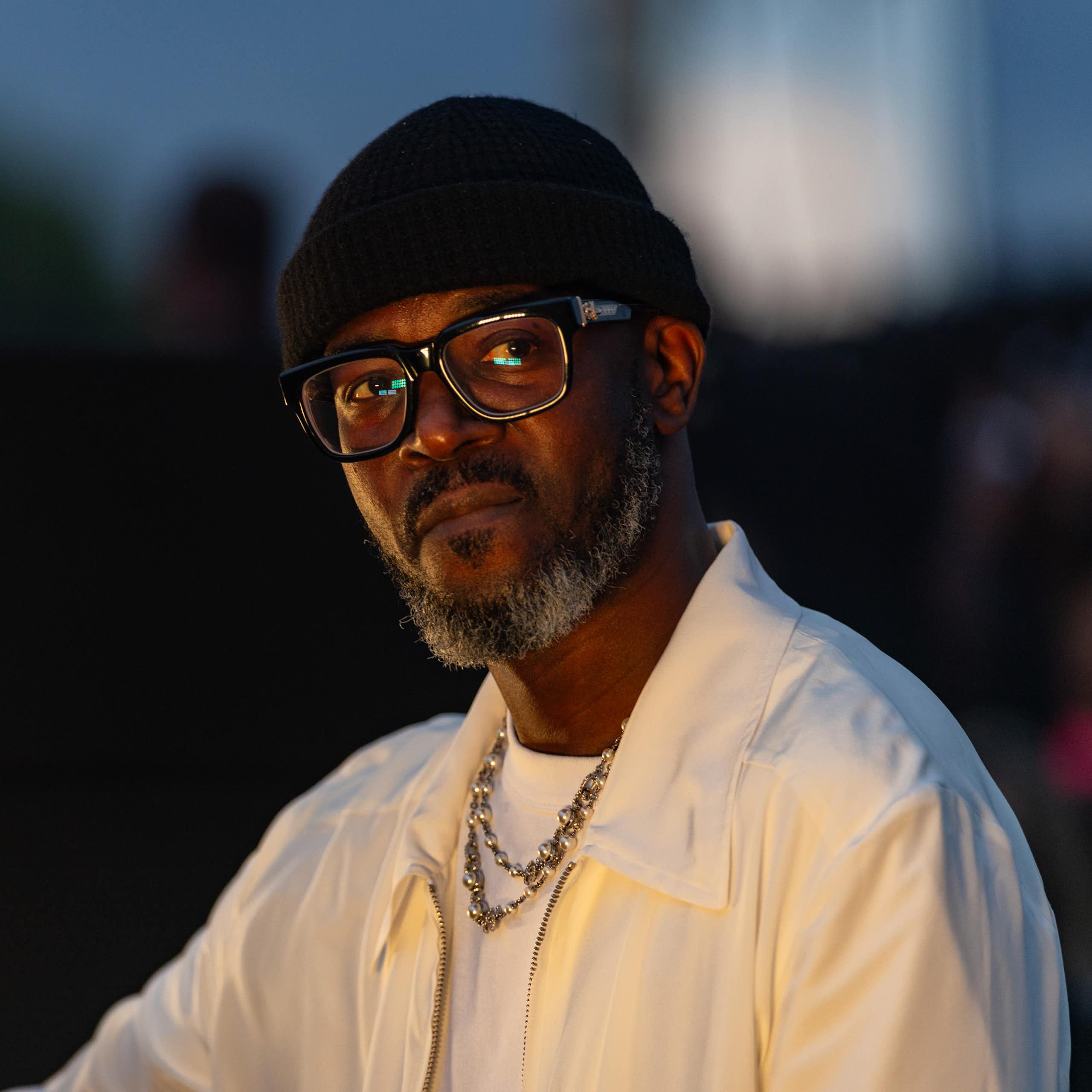 An African man in a beanie and glasses looks ponderous in a photo.