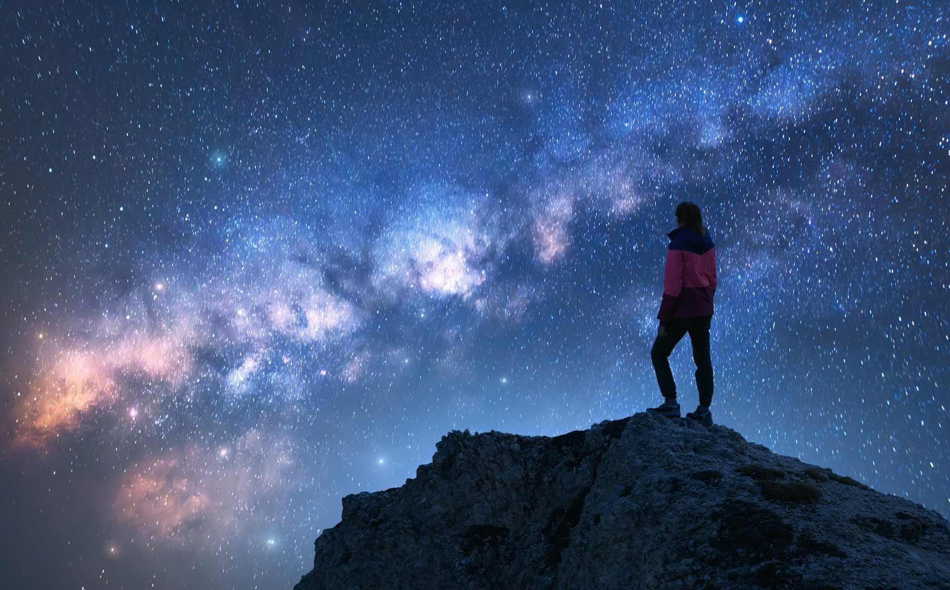 Glowing Milky Way and woman on mountain peak at starry night.
