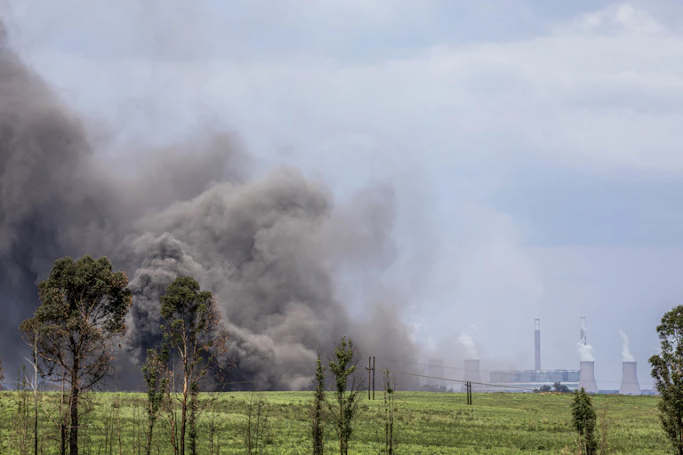 Huge grey cloud of dust rises into the air; in the distance are power station cooling towers