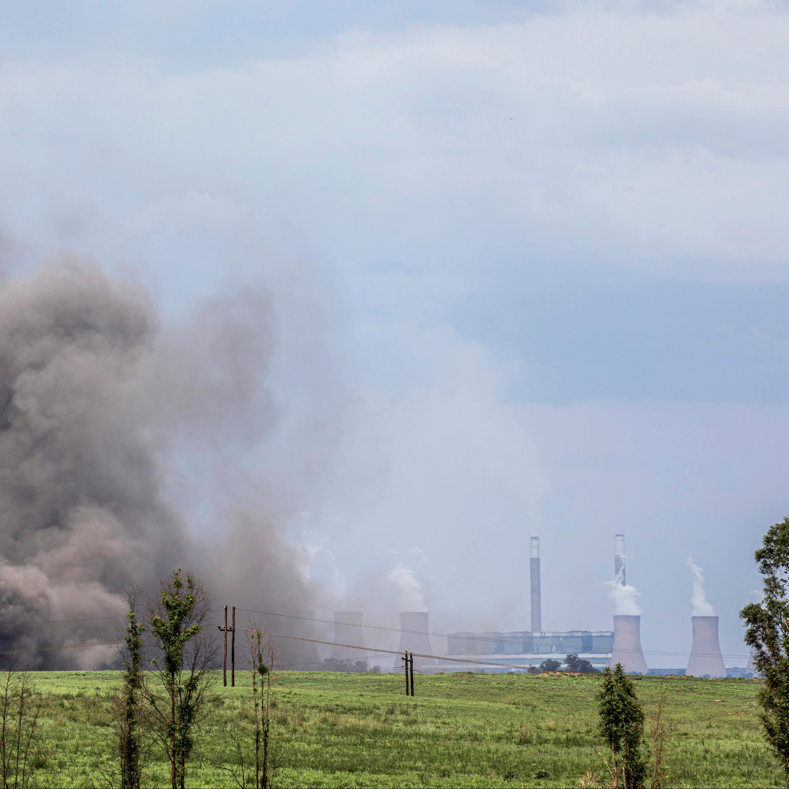 Huge grey cloud of dust rises into the air; in the distance are power station cooling towers