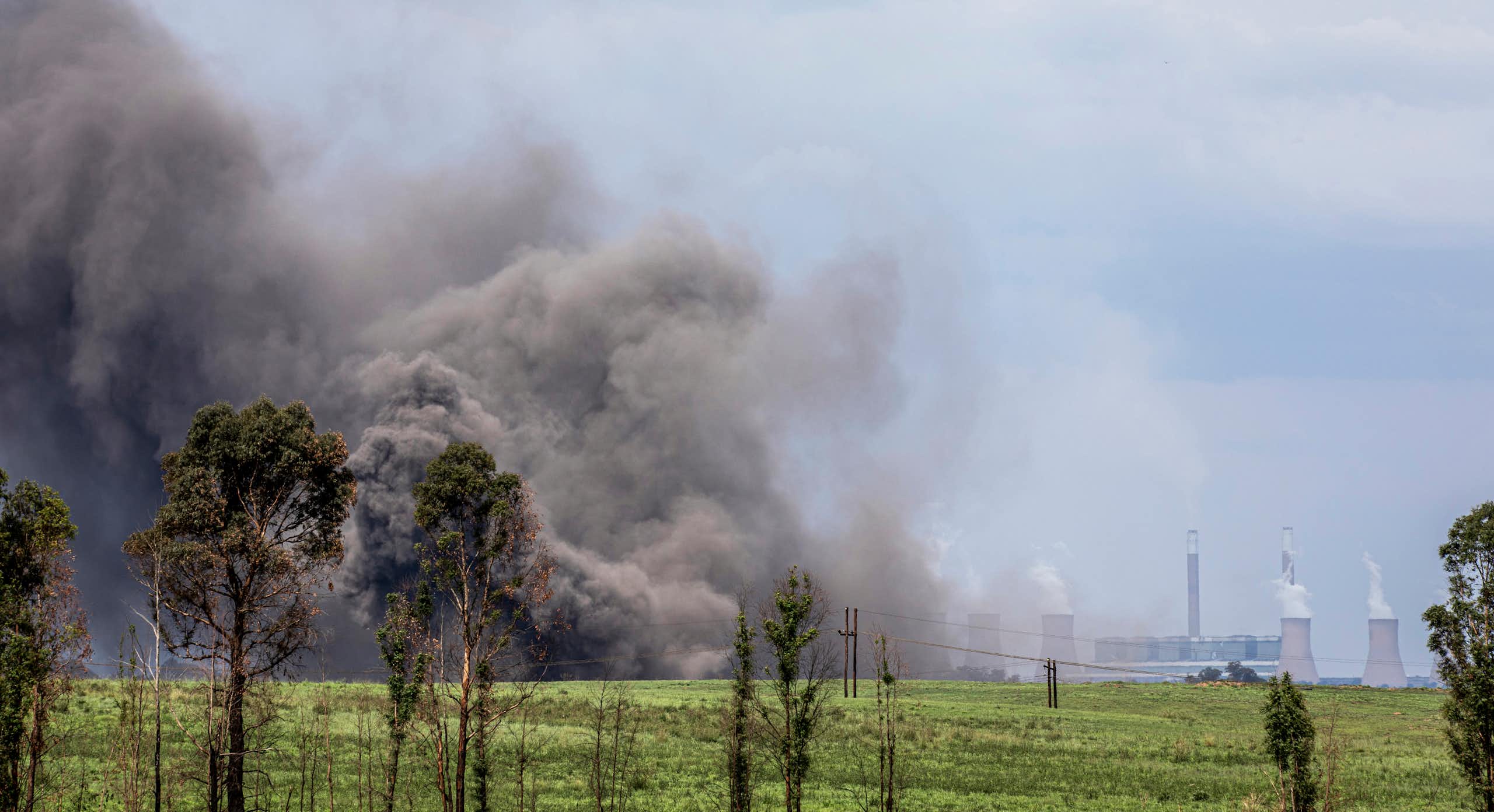 Huge grey cloud of dust rises into the air; in the distance are power station cooling towers