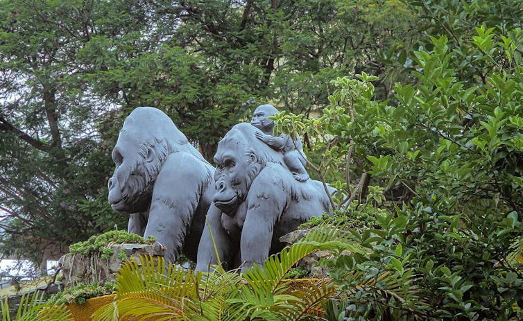 A statue in a breen-leafed area of a male, female, and baby gorilla.