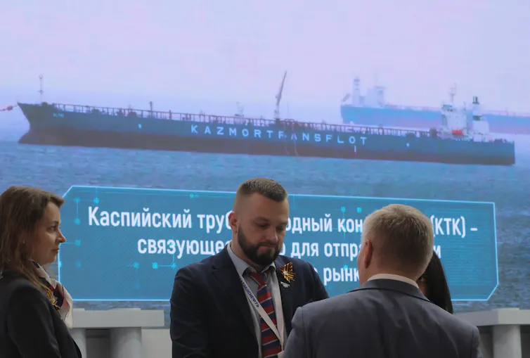 A group of people in suits in front of a picture of an oil tanker.