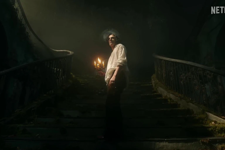 Un hombre con camisa blanca sube una escalera iluminándose con un candelabro.