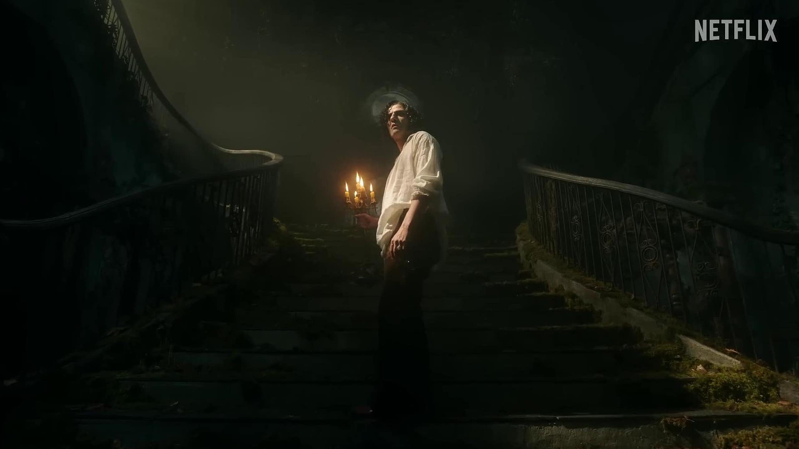 Un hombre con camisa blanca sube una escalera iluminándose con un candelabro.