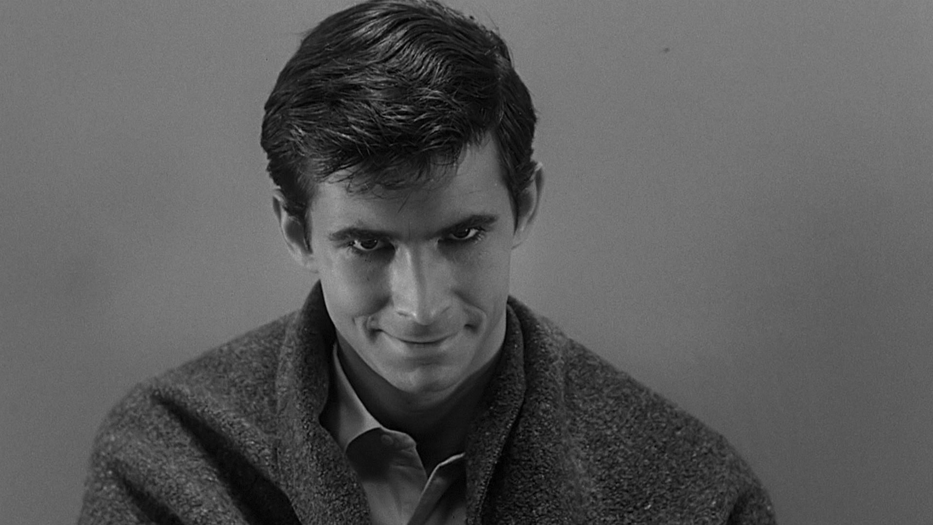 Un hombre mira a la cámara con la cabeza gacha y sonríe.