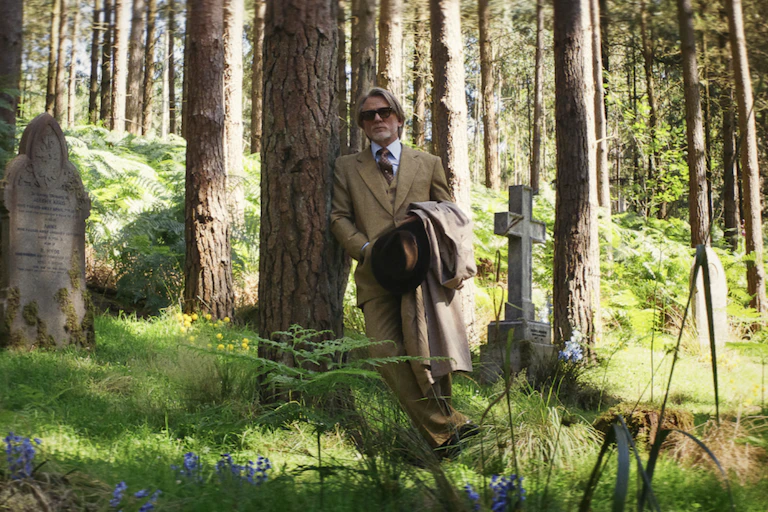 A man in sunglasses standing in a sunlit wood.