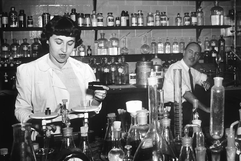 Researchers weigh out chemicals amidst an array of beakers in a laboratory