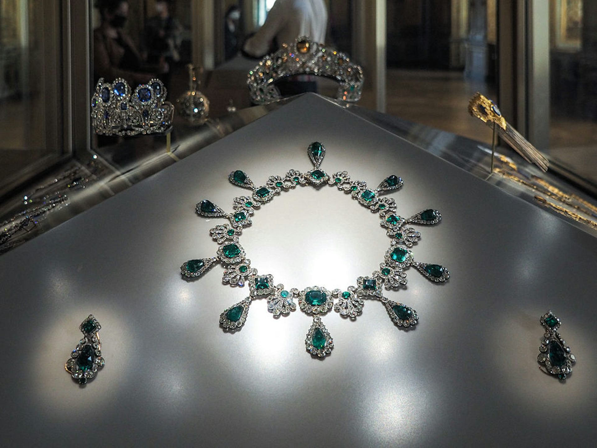 A display case featuring an emerald-and-diamond necklace and a pair of emerald-and-diamond earrings.