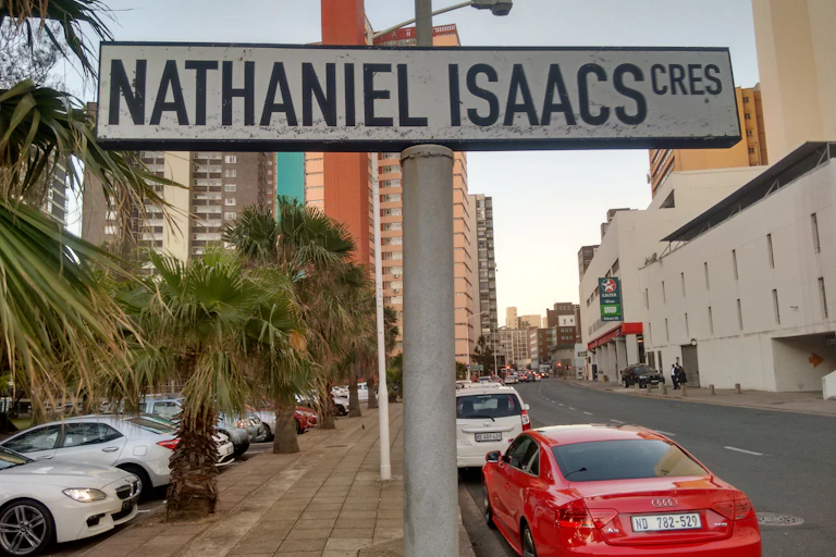 A sign saying 'Nathaniel Isaacs Cres' stands on a road with cars and high-rises in the background.