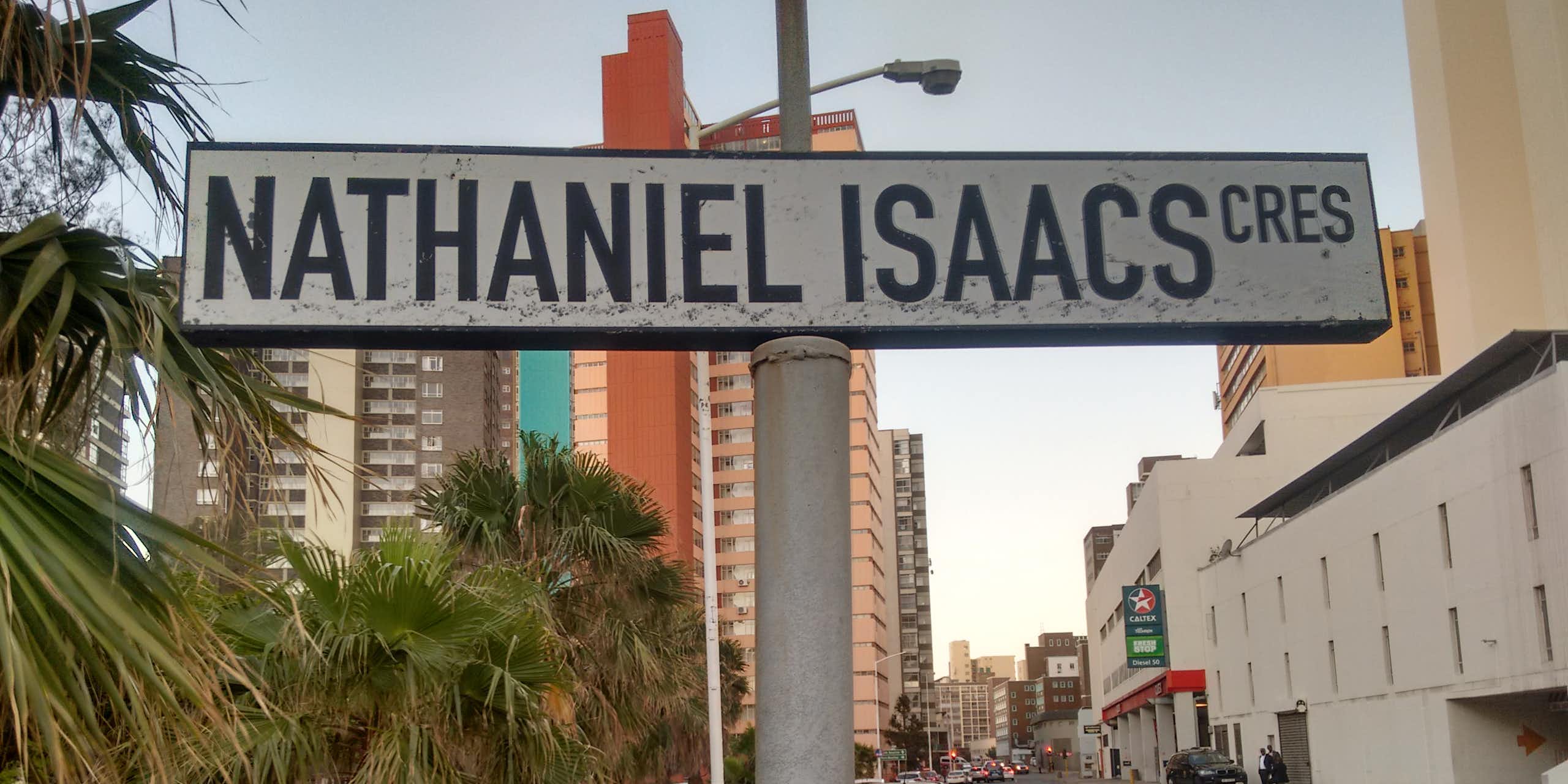 A sign saying 'Nathaniel Isaacs Cres' stands on a road with cars and high-rises in the background.