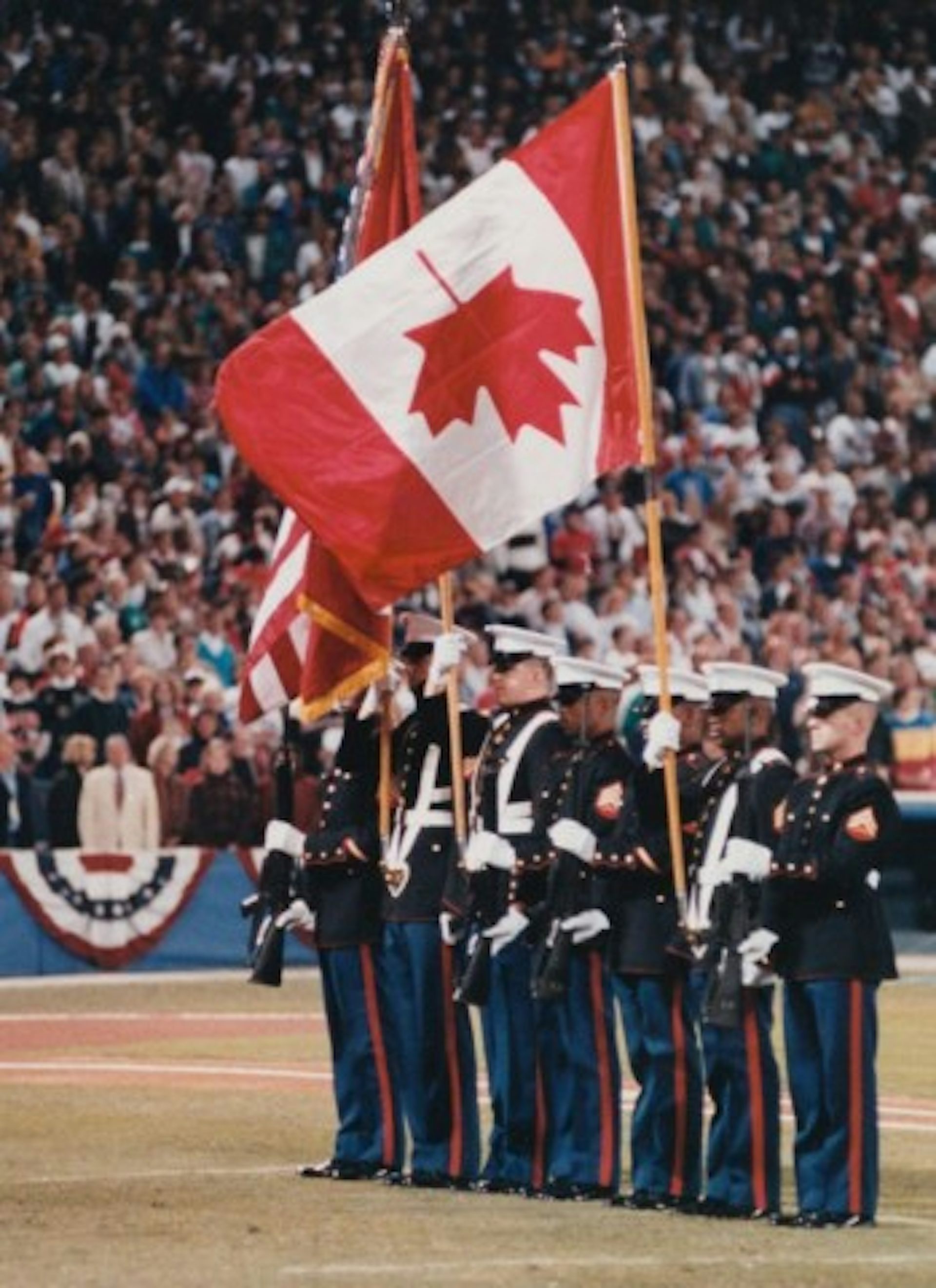 Una fila de soldados sosteniendo banderas. Uno sostiene un asta de bandera con la bandera canadiense al revés