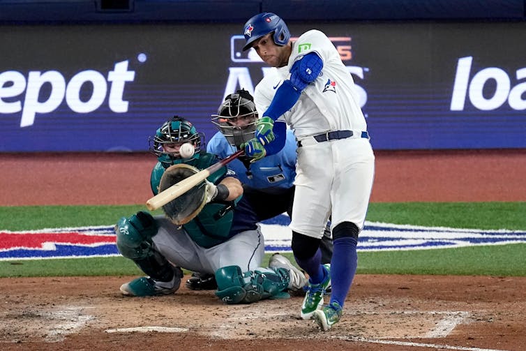 La fiebre de los Azulejos está surgiendo mientras Canadá se prepara para la Serie Mundial por primera vez en 32 años. 4 Un jugador de béisbol con uniforme blanco y azul balancea el bate en el campo, preparándose para hacer contacto con todos