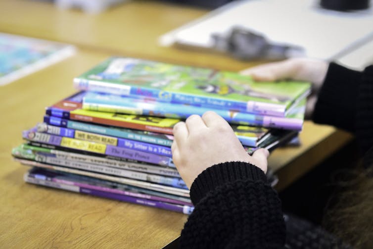 A person's hands partially cover a stack of children's books.