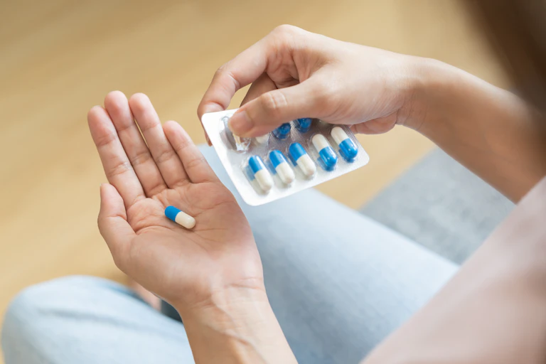 Uma pessoa segura na mão um comprimido que retirou de uma embalagem blister do mesmo medicamento.