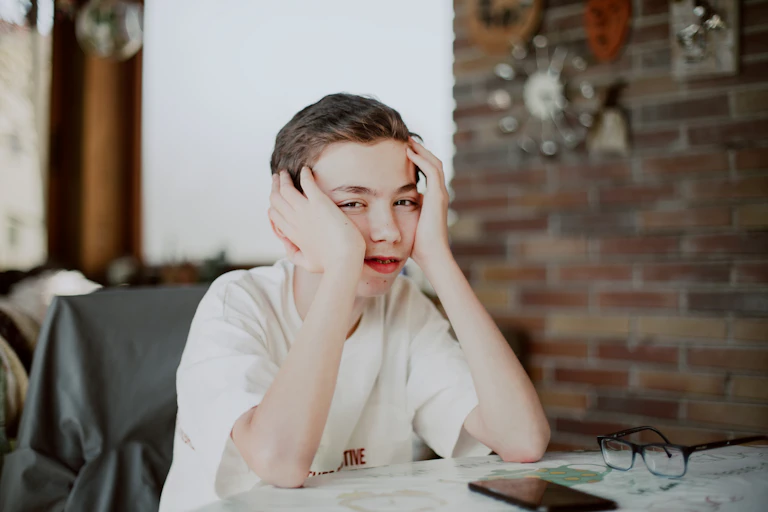 Bored teen boy rests his head on his hands.