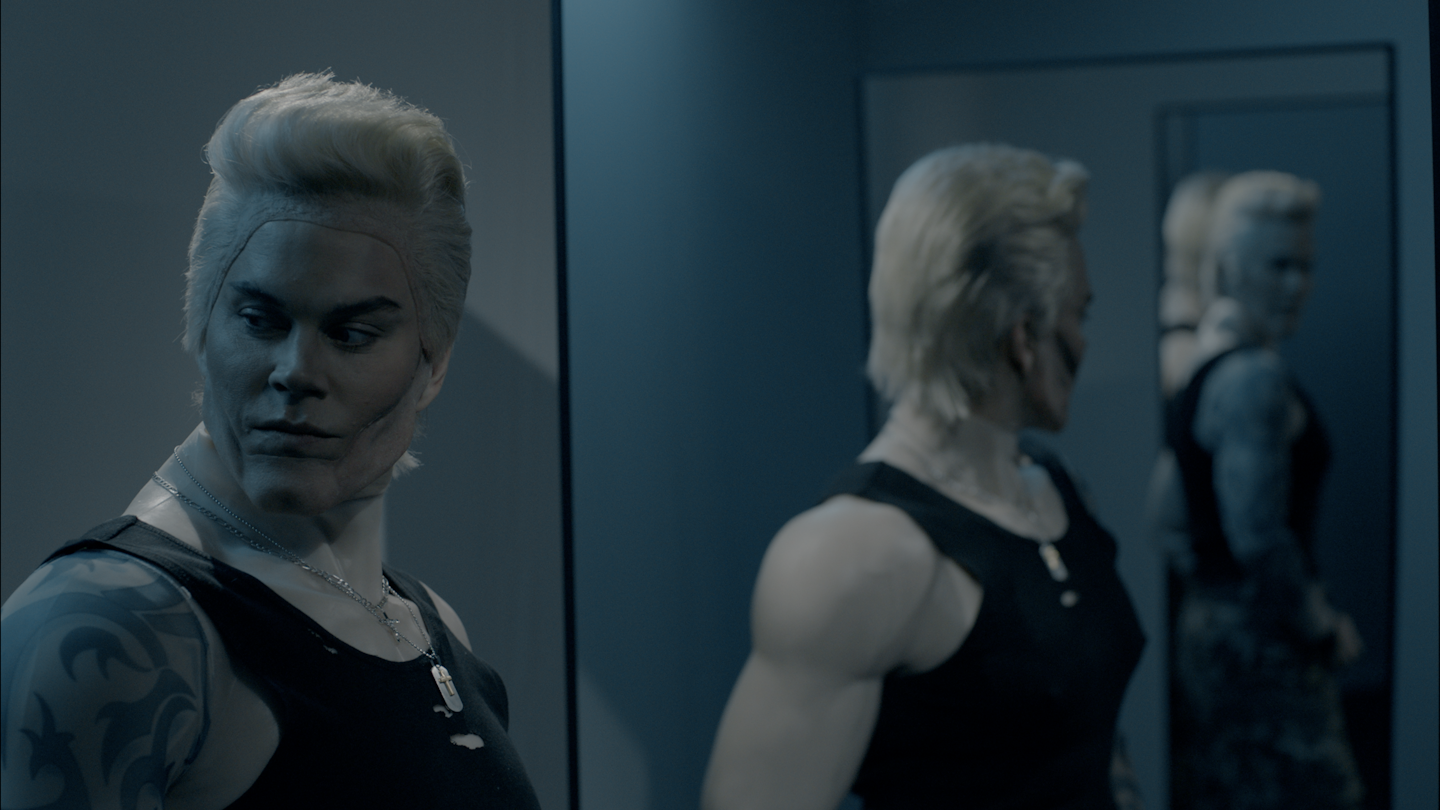Actor in prosthetics to appear as a muscular, blonde man looking in the mirror