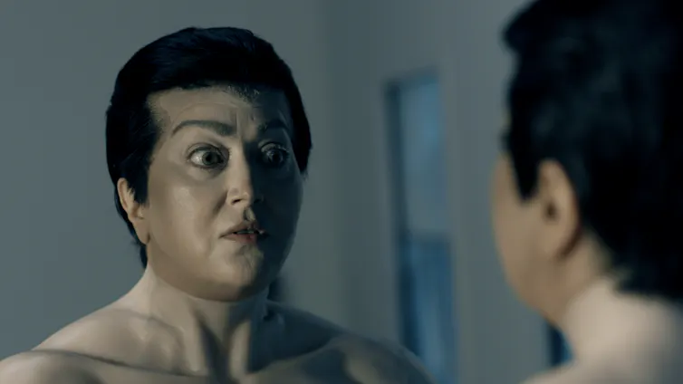A weird looking man looks into a mirror.