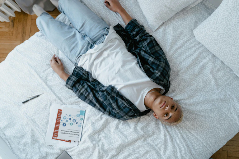 A young person lies on a bed, staring at the ceiling.