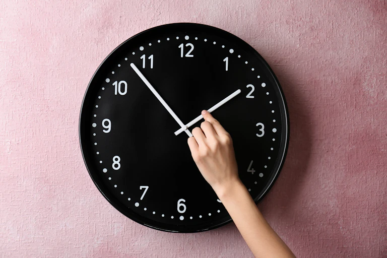 Una mano cambia la hora en un reloj de pared.