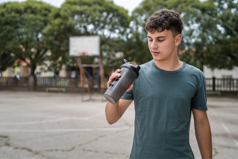 A young man holds a supplement shaker and looks into it.