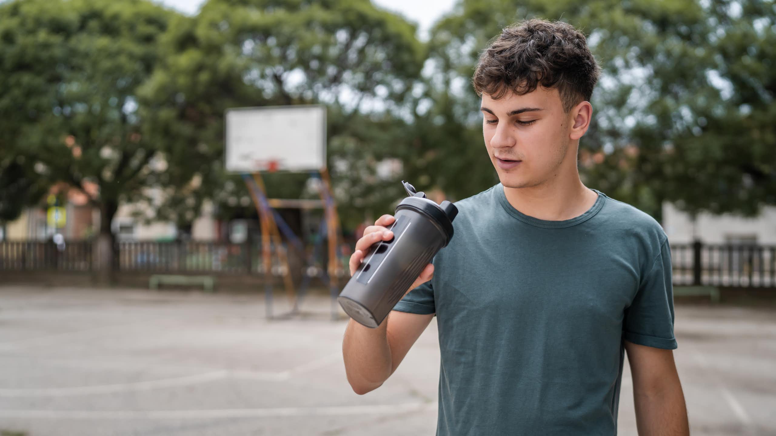 A young man holds a supplement shaker and looks into it.