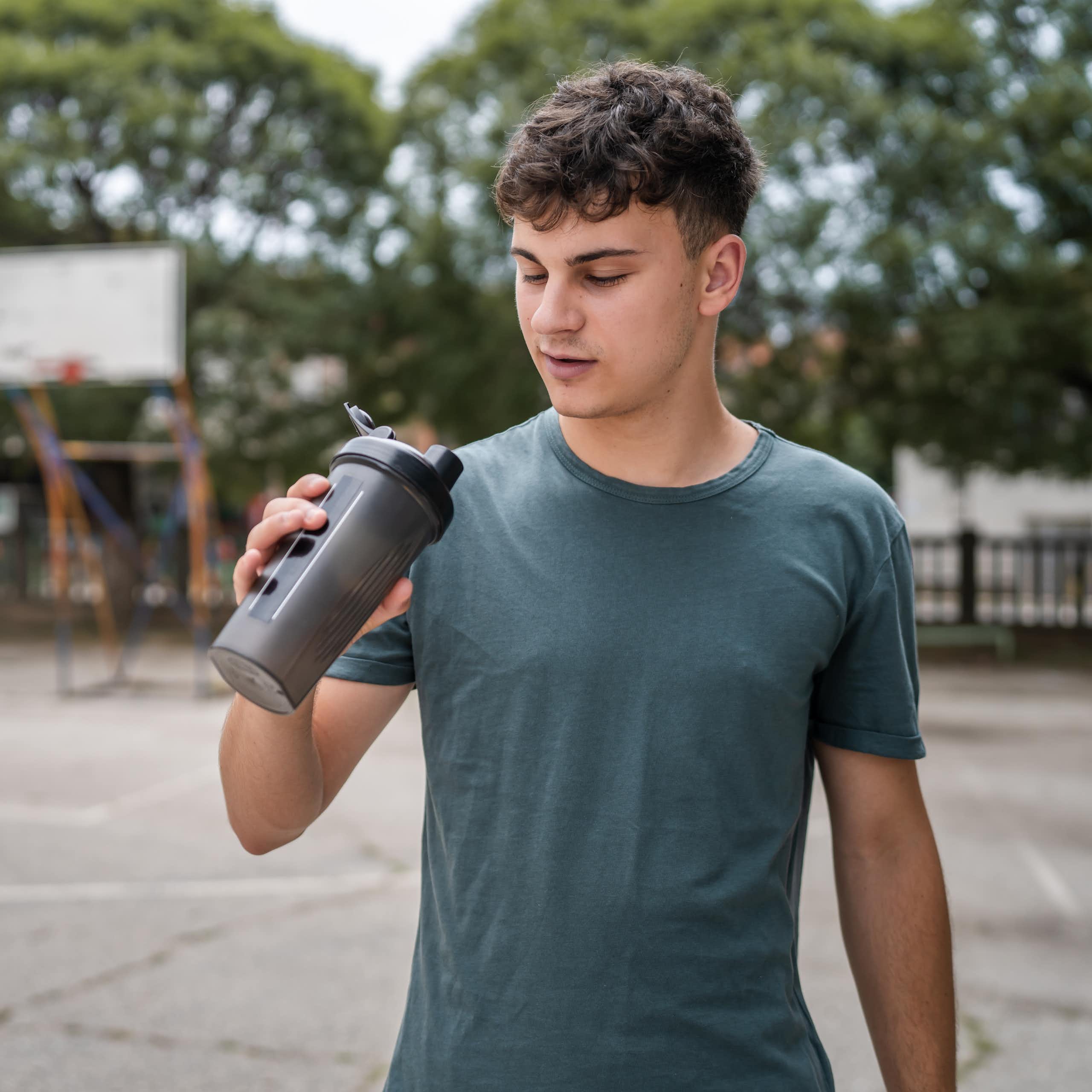 A young man holds a supplement shaker and looks into it.