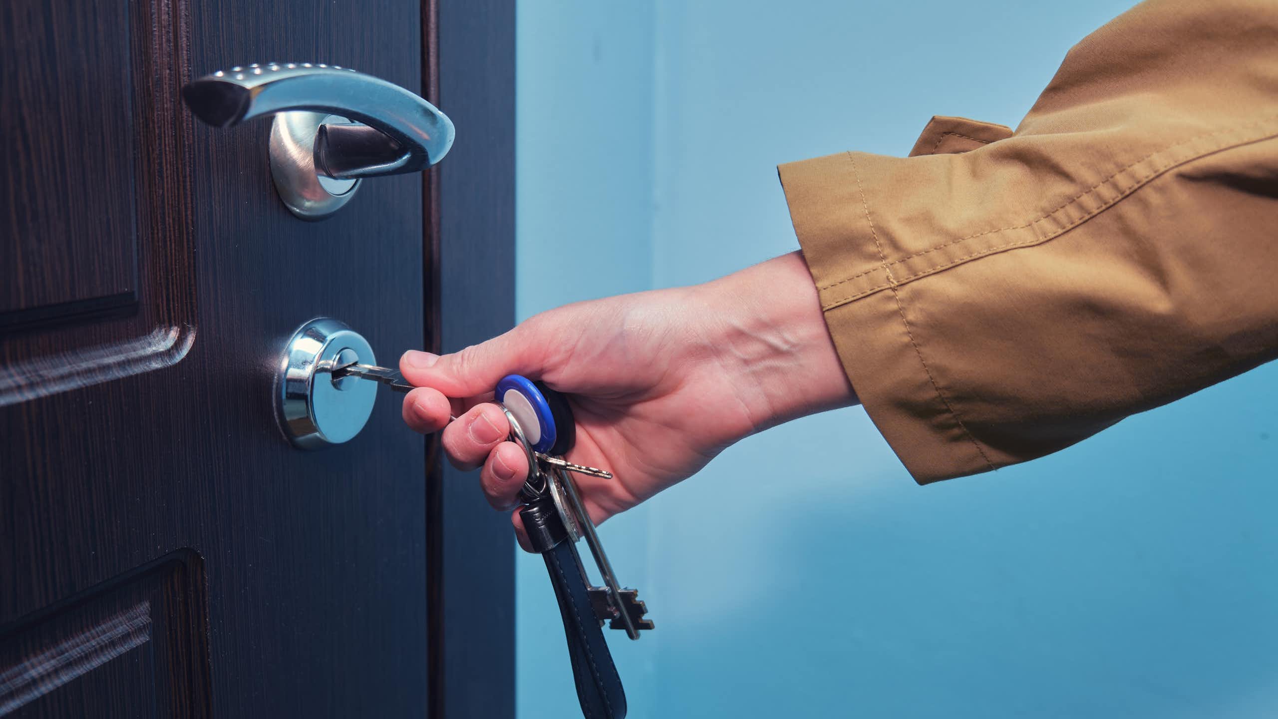 A hand inserting a key into the lock of a front door