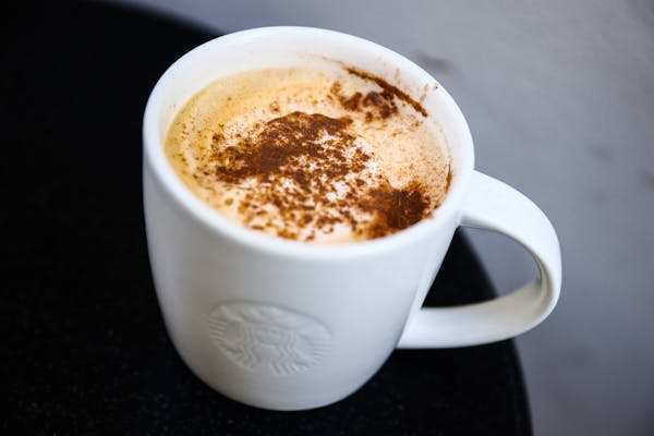 A white mug with a Starbucks logo, filled with foamy coffee and powdered cinnamon on top.