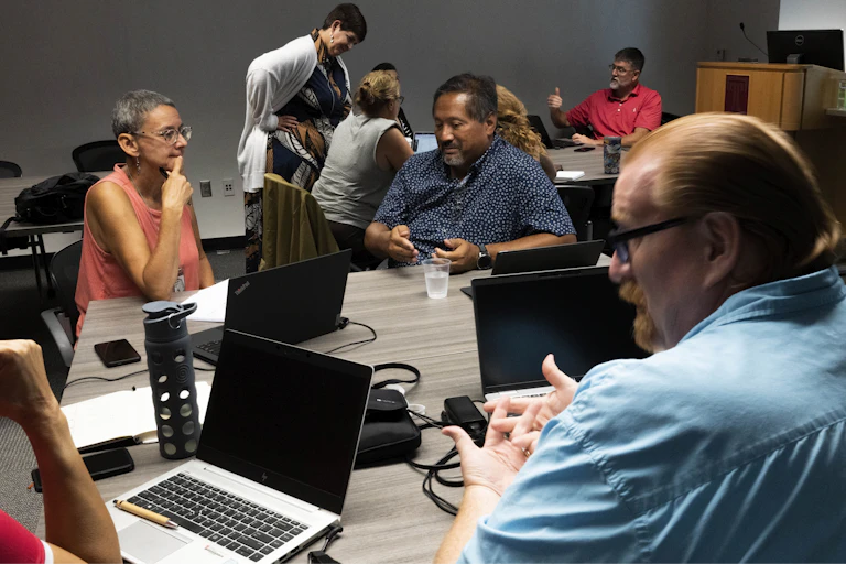 Group of teachers with laptops to discuss AI policies.