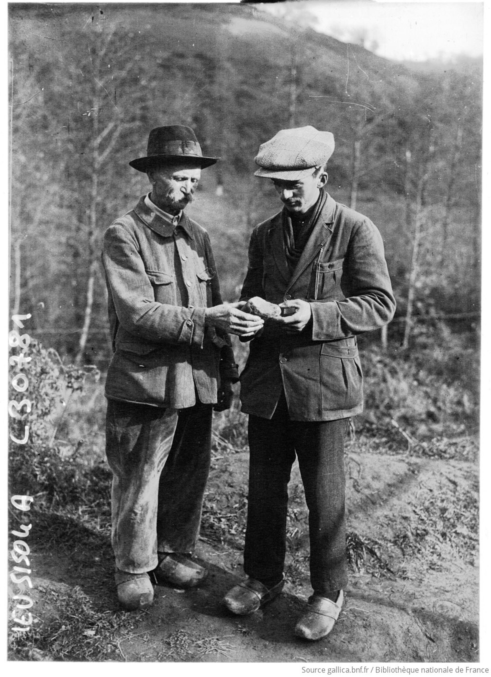 two men in jackets and caps hold and examine an object outdoors