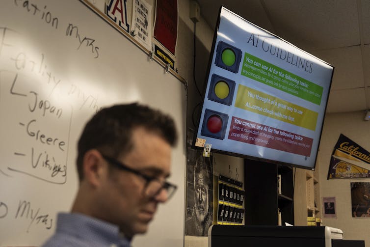 Un profesor sentado al frente de la clase con políticas de IA publicadas en la pantalla encima de él.