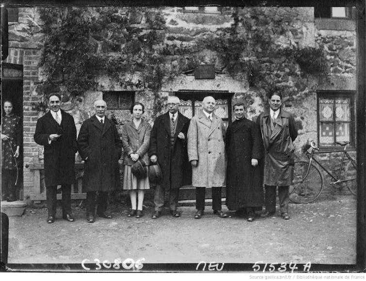Siete personas vestidas formalmente se encuentran junto al edificio.