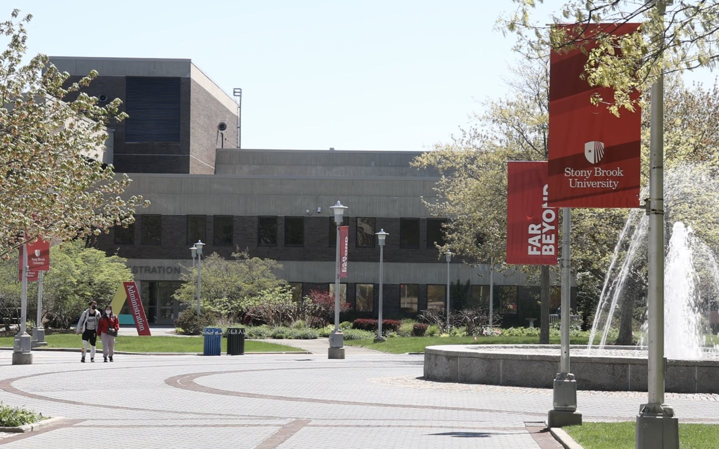 A gray building is seen with red signs hanging nearby that say 'Stony Brook University.'