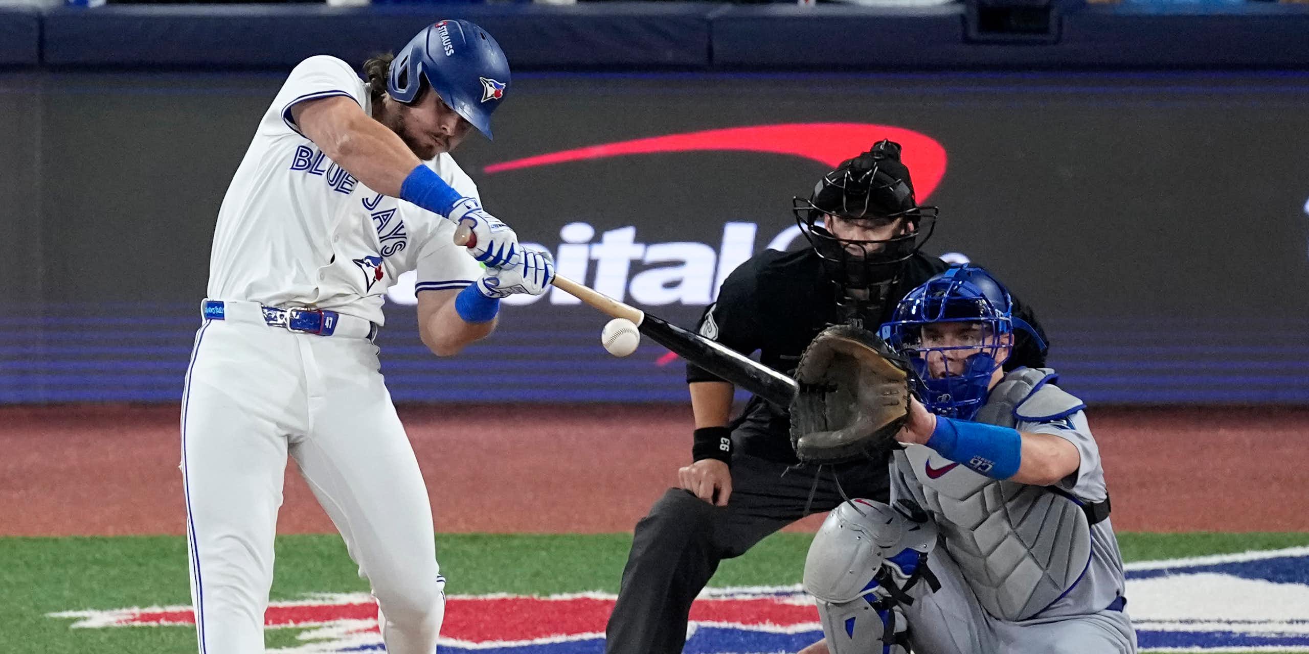 A man in a Blue Jay uniform swings at an approaching ball.