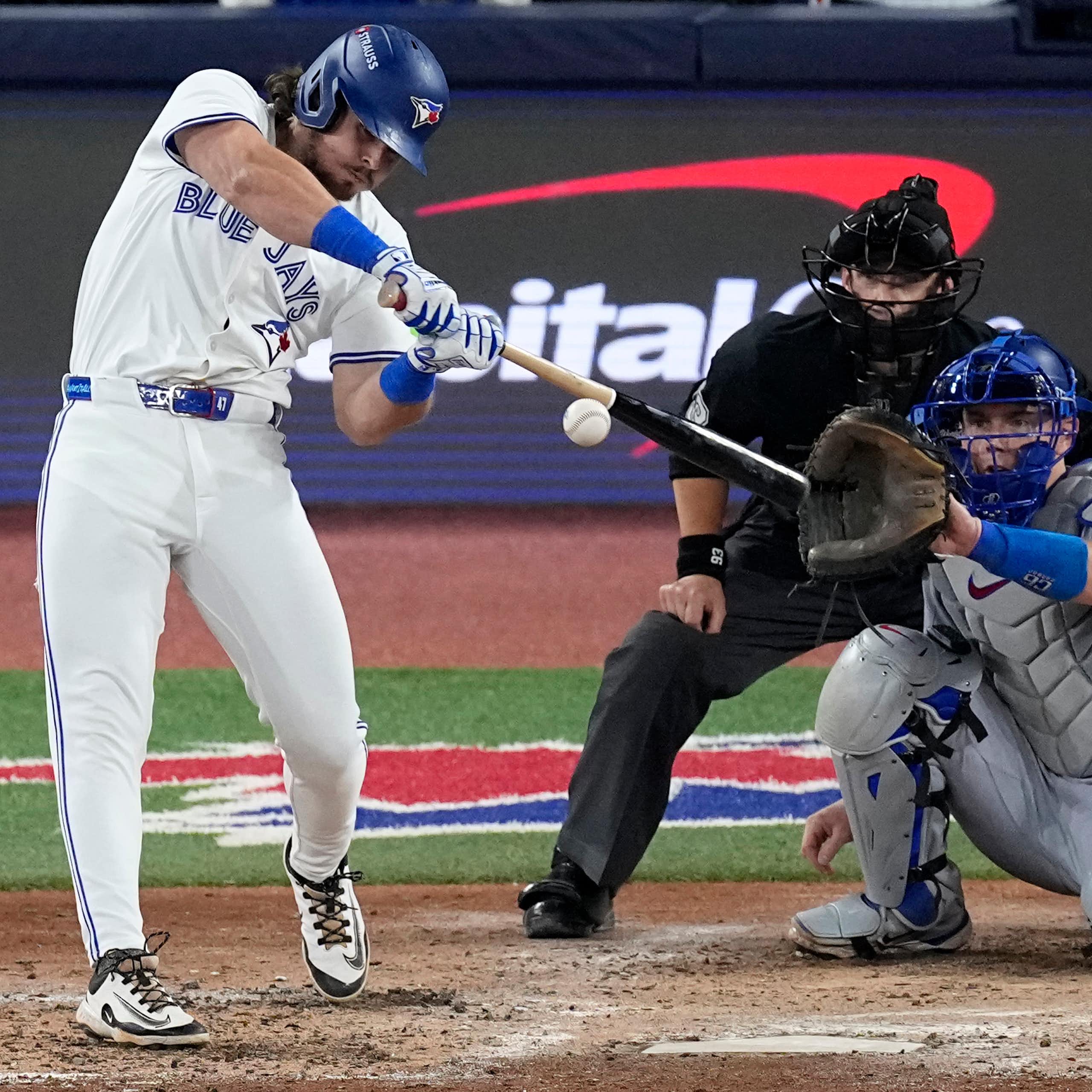A man in a Blue Jay uniform swings at an approaching ball.