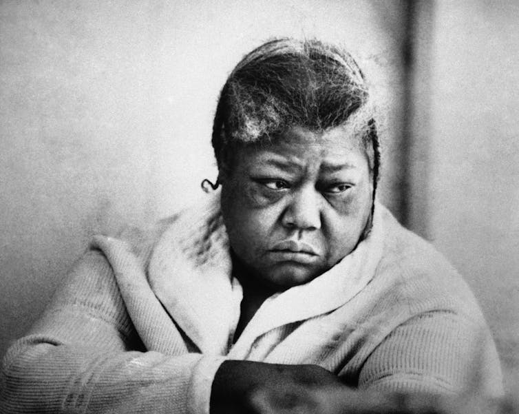 A Black woman wearing a bathrobe looks to her left with a serious expression.